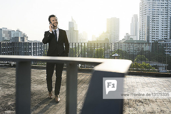 Business man in dark suit speaking into smartphone on city rooftop