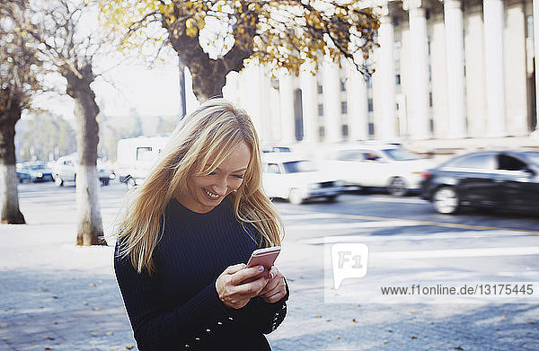 Lächelnde blonde Frau mit Smartphone in der Stadt