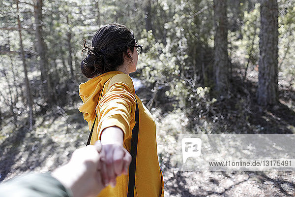 Junges Mädchen mit gelbem Pullover hält Hand eines Mannes im Wald