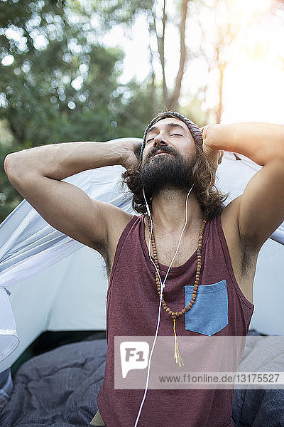 Portrait of man in front of tent listening music with earphones