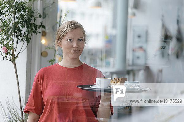 Porträt einer jungen Frau  die in einem Café Kaffee und Kuchen serviert
