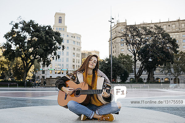 Rothaarige Frau spielt Gitarre in der Stadt