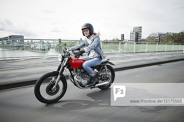 Germany  Cologne  young woman riding motorcycle on bridge