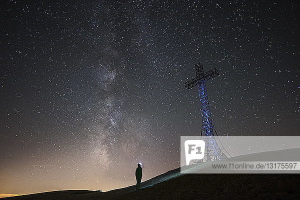 Italien  Marken  Silhouette eines Mannes  der nachts das Gipfelkreuz auf dem Monte Catria betrachtet