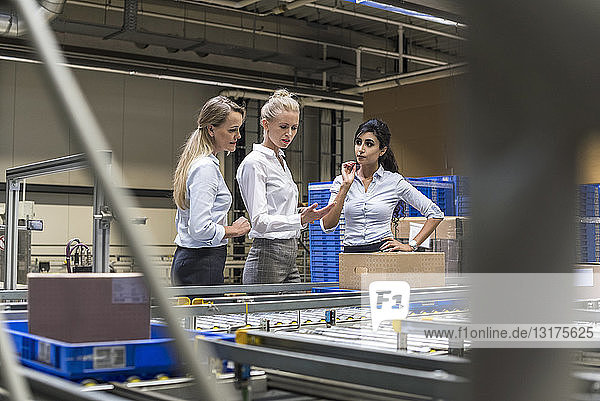 Three women discussing at conveyor belt in factory