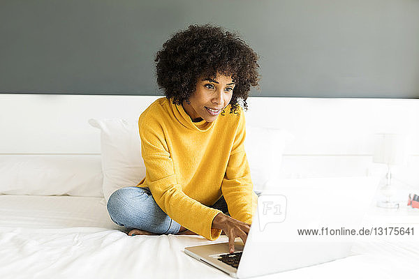 Lächelnde Frau sitzt mit Laptop auf dem Bett