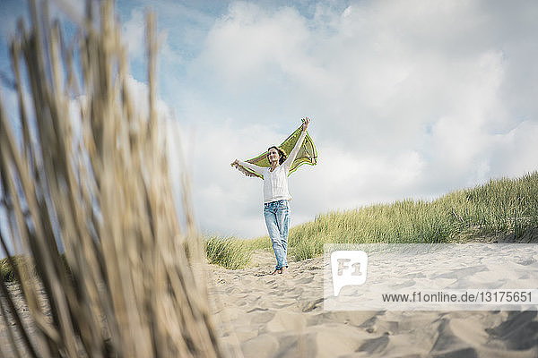 Reife Frau hält flatterndes Tuch im Wind  Relaxiang in den Dünen