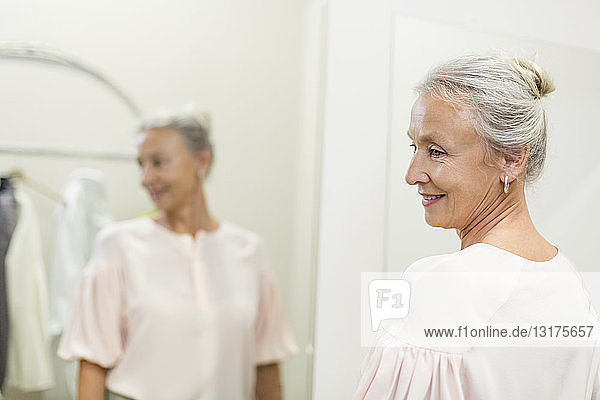 Lächelnde ältere Frau in einer Boutique  die sich im Spiegel spiegelt