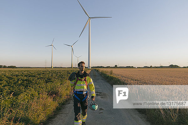 Techniker  der mit Kletterausrüstung einen Feldweg an einem Windpark begeht