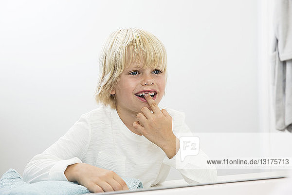 Lächelnder Junge schaut in den Badezimmerspiegel und untersucht seine Zahnlücke