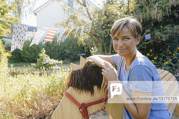 Portrait of smiling woman with wood horse in garden