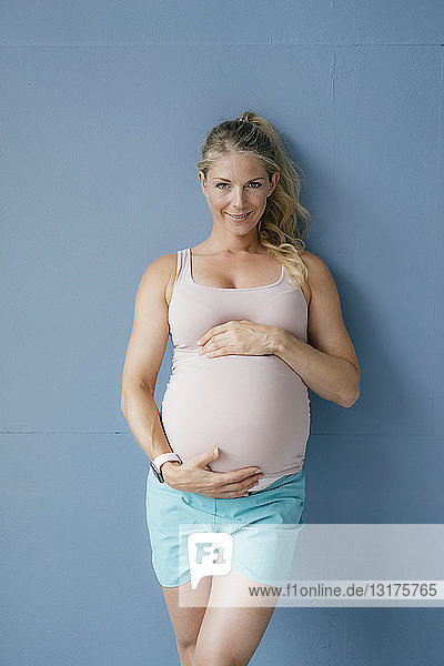 Porträt einer lächelnden schwangeren Frau an blauer Wand stehend