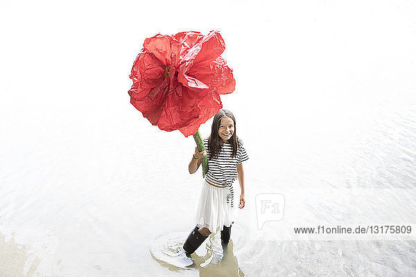 Porträt eines lächelnden Mädchens  das in einem See steht und eine überdimensionale rote Kunstblume hält