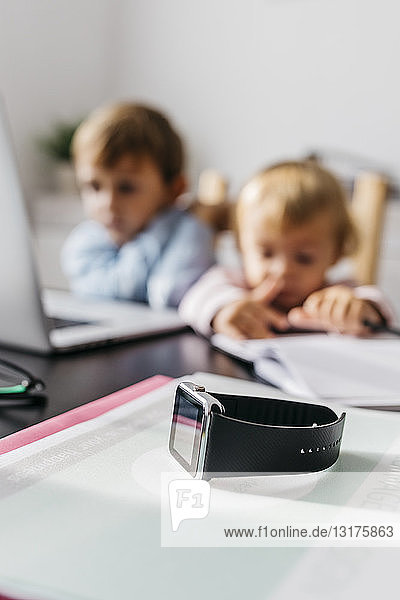 Smartwatch auf einem Schreibtisch  im Hintergrund Kinder mit Laptop