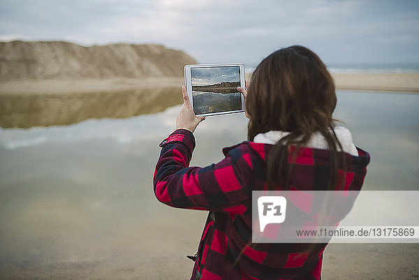 Junge Frau fotografiert mit Tablette am Strand