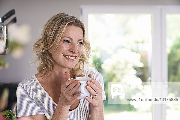 Porträt einer lächelnden Frau  die in der Küche Kaffee trinkt