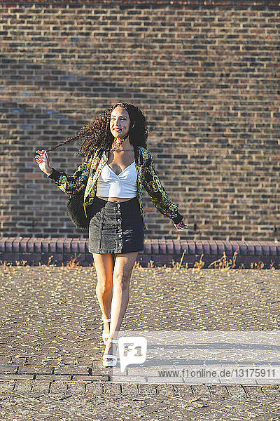Smiling young woman with curly hair walking in front of brick wall