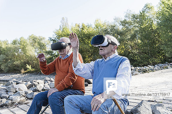 Two old friends sitting by the riverside  using VR glasses