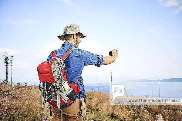 Mann fotografiert mit seinem Handy während einer Wanderung
