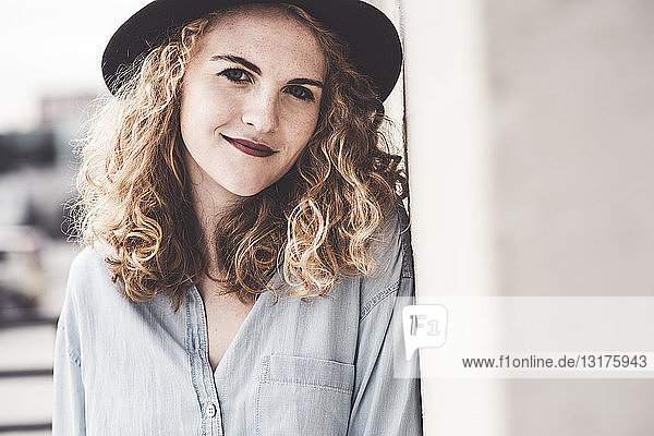 Portrait of smiling young woman wearing hat leaning against wall