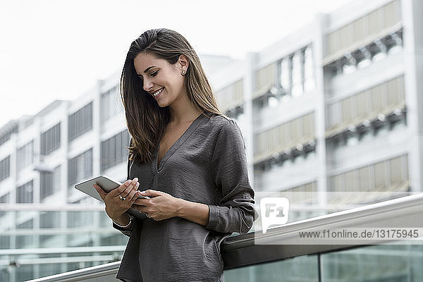 Lächelnde junge Geschäftsfrau benutzt digitales Tablet im Freien