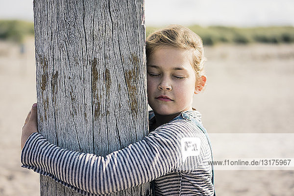 Kleines Mädchen umarmt Holzstange mit geschlossenen Augen