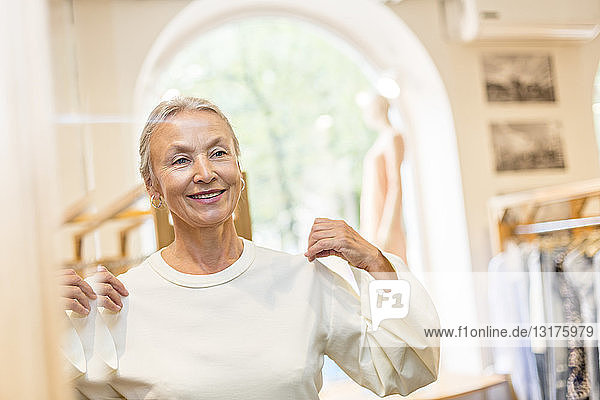 Lächelnde ältere Frau beim Anprobieren eines Pullovers in einer Boutique