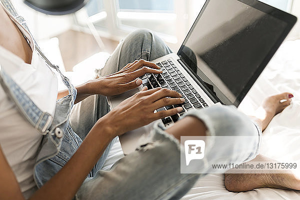 Close-up of woman sitting on bed using laptop