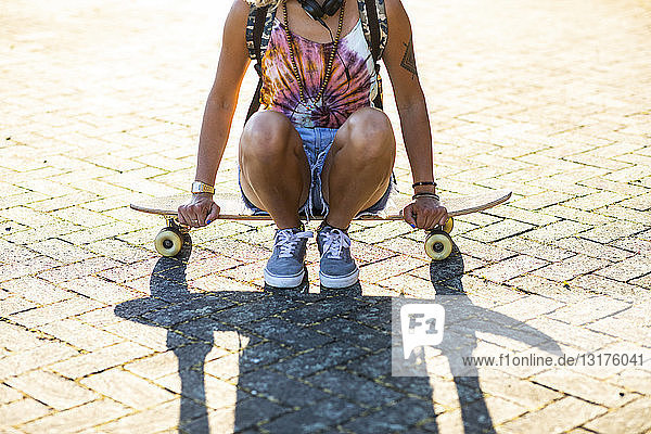 Nahaufnahme einer jungen Frau  die im Sonnenlicht auf einem Skateboard sitzt
