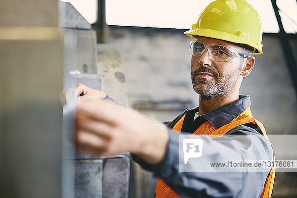 Porträt eines selbstbewussten Mannes in Arbeitsschutzkleidung bei der Arbeit in einer Fabrik