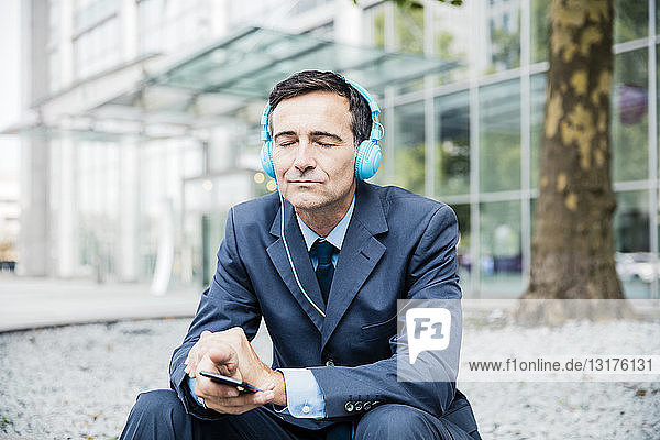 Geschäftsmann mit geschlossenen Augen  der in der Stadt mit Kopfhörern Musik hört