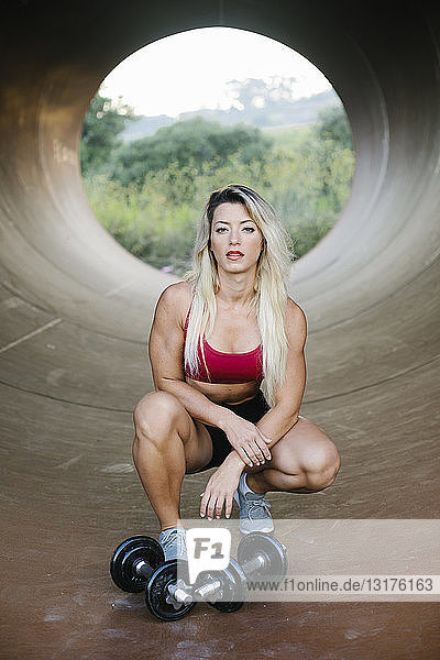 Athletic woman crouching inside a tube with dumbbells