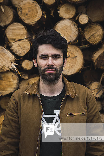 Portrait of young man in front of of stack of wood