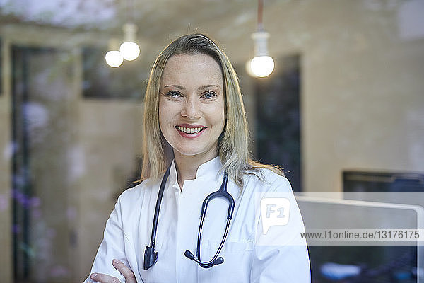 Porträt einer lächelnden Ärztin mit Stethoskop hinter Fensterscheibe