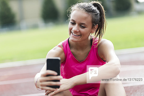 Teenage girl sitting on race track  using smartphone