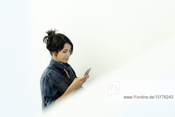 Dunkelhaarige Frau im Jeanshemd beim Blick auf ihr Handy
