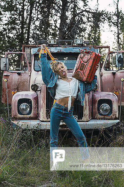 Junge Frau posiert an einem kaputten Oldtimer-LKW  der einen Benzinkanister hält