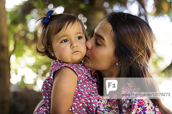 Young woman kissing serious looking baby girl