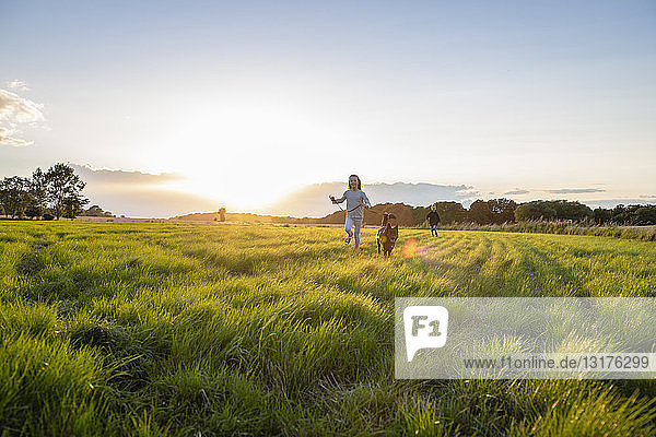 Zwei Kinder mit einem Hund laufen bei Sonnenuntergang über ein Feld