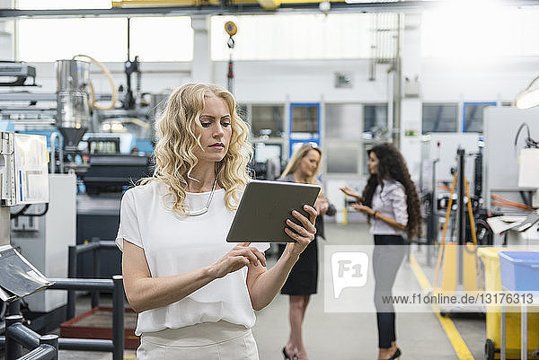 Woman using tablet in factory shop floor with two women in background
