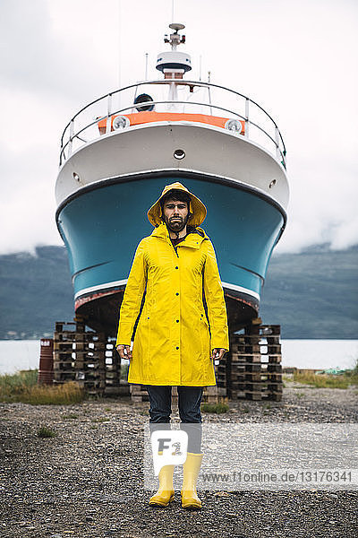 Junger Mann steht vor einem Schiff und trägt Regenkleidung  Lappland  Norwegen