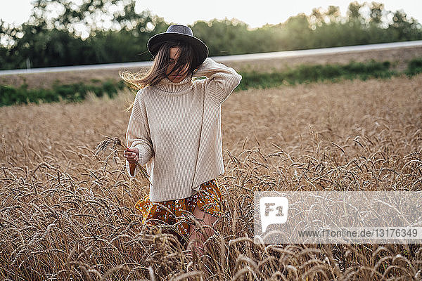 Junge Frau mit Hut und übergroßem Rollkragenpullover geht im Maisfeld spazieren