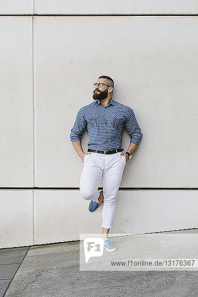 Bearded hipster businessman wearing glasses and plaid shirt leaning against wall
