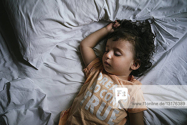 Mädchen schläft im Bett mit T-Shirt-Botschaft 'Träume werden doch wahr'.