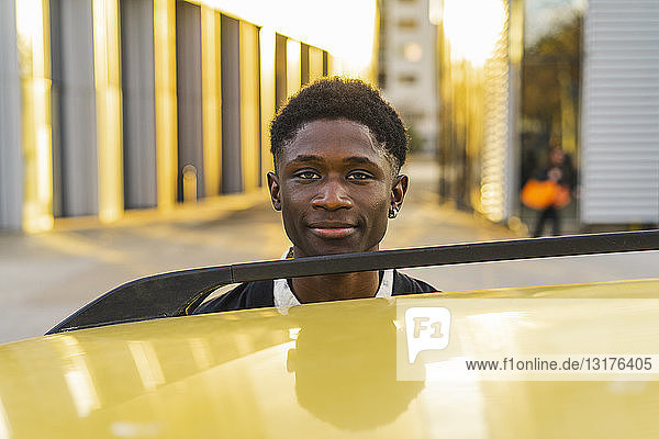 Porträt eines schwarzen jungen Mannes  der an einem Auto steht