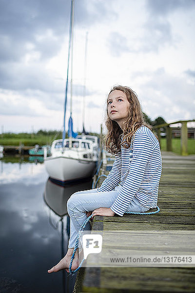 Mädchen sitzt auf einem Steg in einem kleinen Hafen