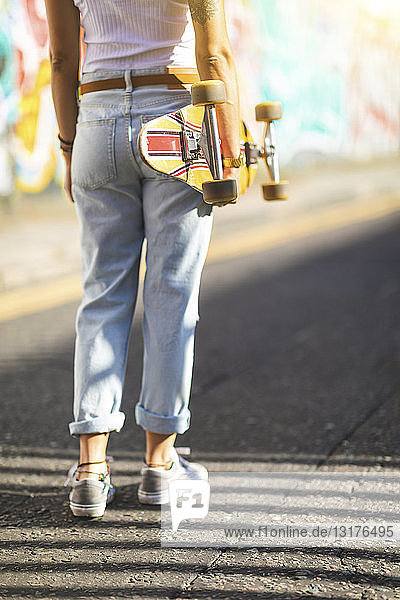 Rückansicht einer jungen Frau mit Skateboard in der Stadt