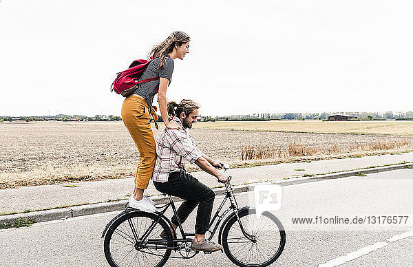 Glückliches junges Paar fährt gemeinsam auf einem Fahrrad auf der Landstraße