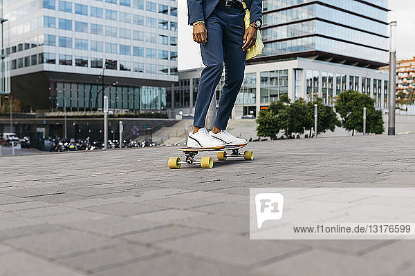 Spanien  Barcelona  Beine eines jungen Geschäftsmannes beim Skateboardfahren in der Stadt