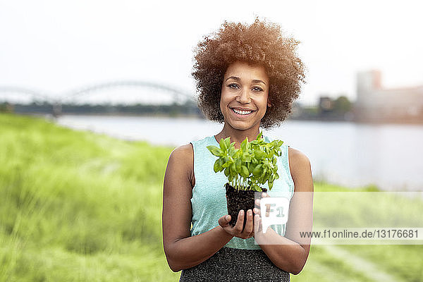 Porträt einer lächelnden Frau  die eine Pflanze im Freien hält